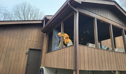 Person in orange safety gear working from an upper-floor window of a brown building