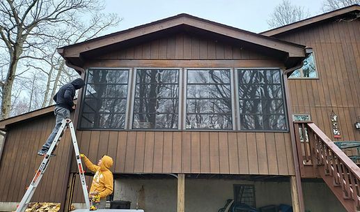 Two people on ladders cleaning the screened front of a brown house