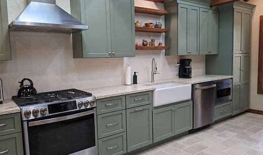 Modern kitchen with sage green cabinets, stainless steel appliances, white farmhouse sink, and tile floor