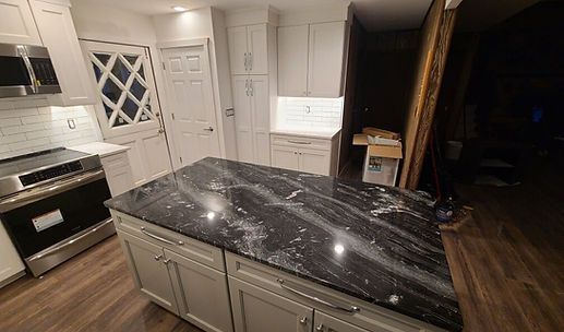 Modern kitchen with a black marble island, white cabinets, and stainless steel appliances.
