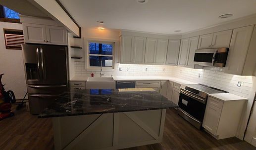 Modern kitchen with dark cabinets, black island countertop, white backsplash, and stainless steel appliances.