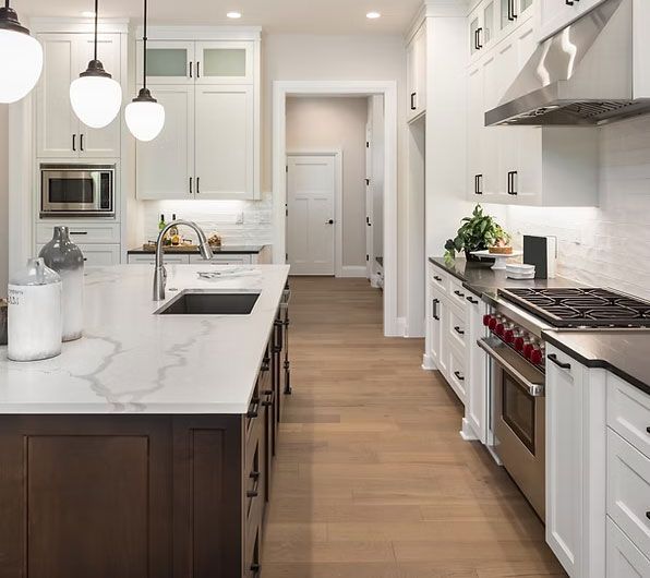 Modern white kitchen with marble island, dark wood cabinets, pendant lights, and stainless steel appliances