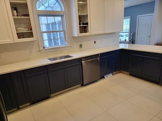 Modern kitchen with dark lower cabinets, white upper cabinets, tiled floor, and a window over the counter.