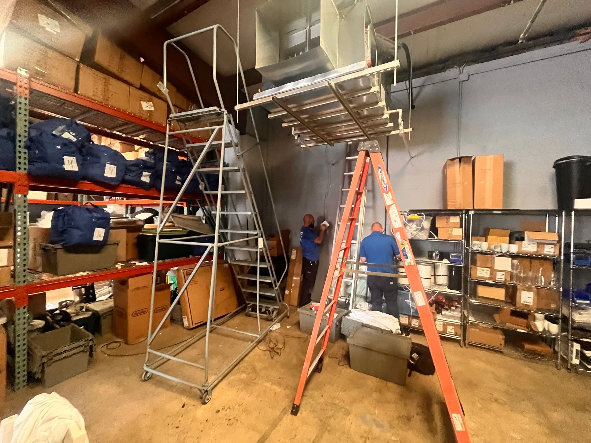 A man is standing on a ladder in a warehouse.