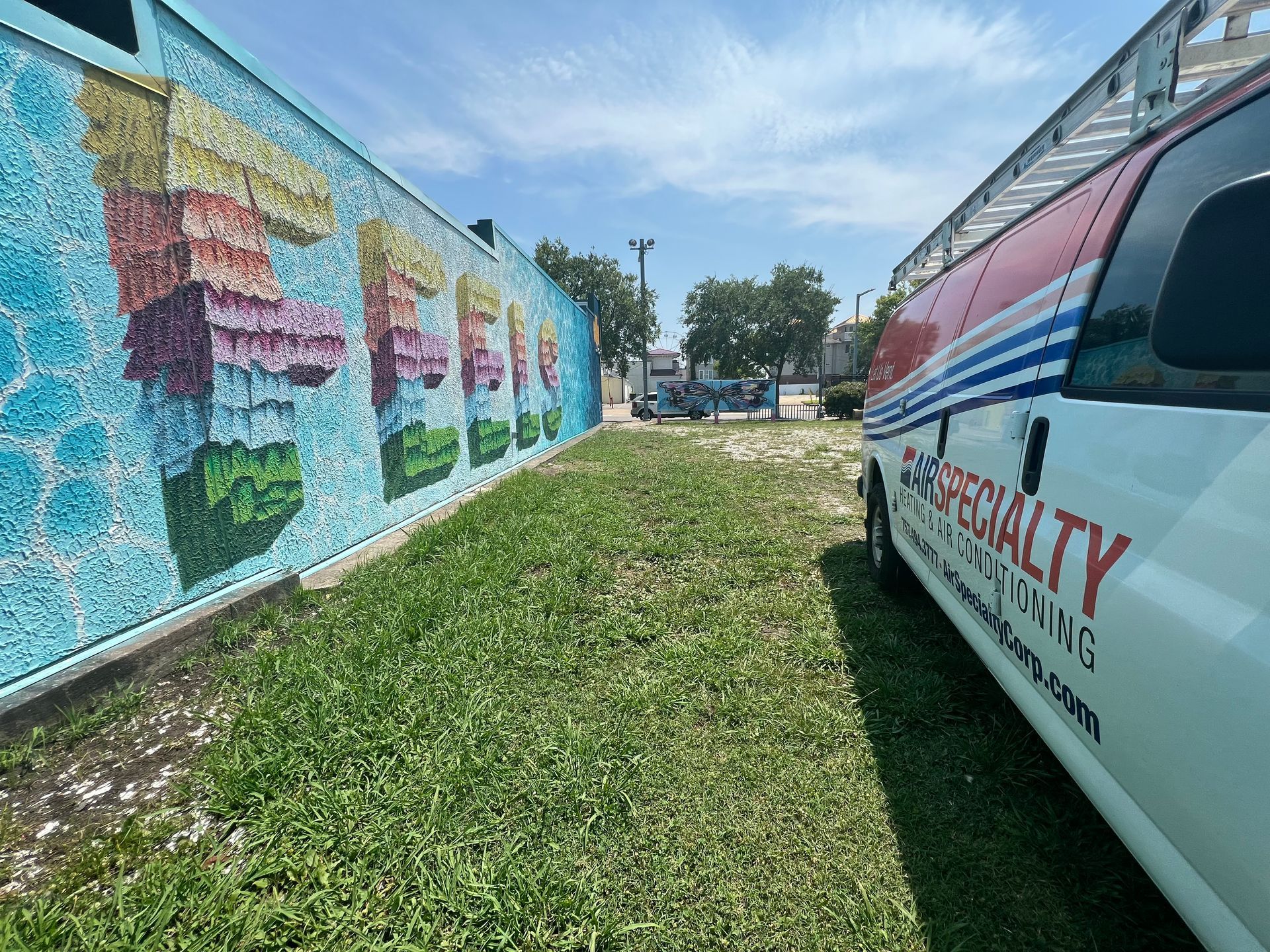 A white van is parked in front of a mural on a wall.