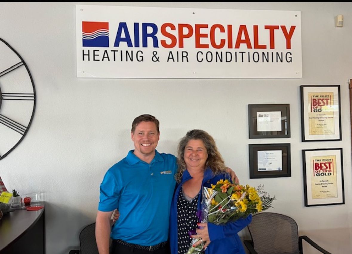 a man and woman are posing in front of a sign that says air specialty heating and air conditioning