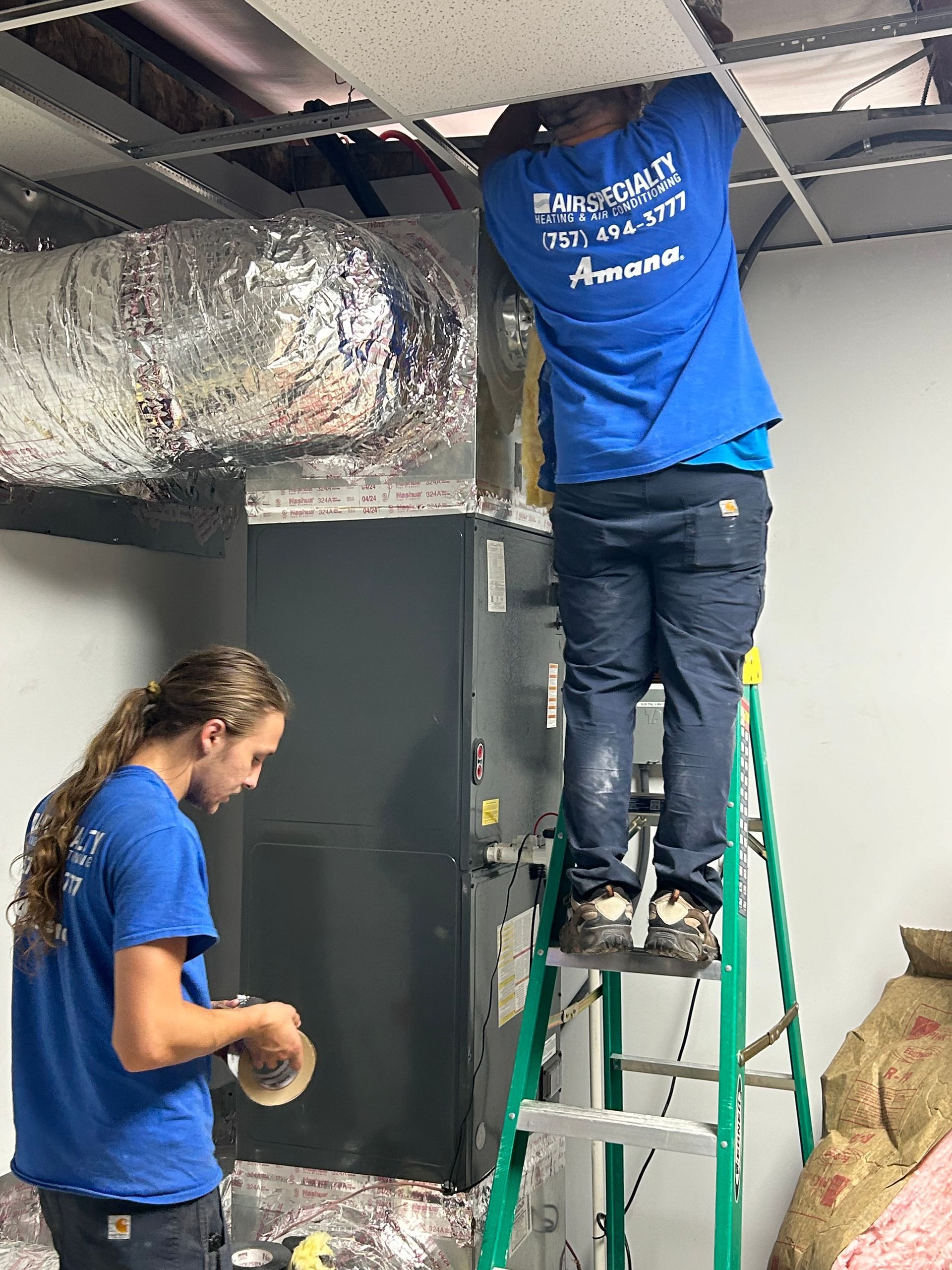 Two men are working on an air conditioner in a room.
