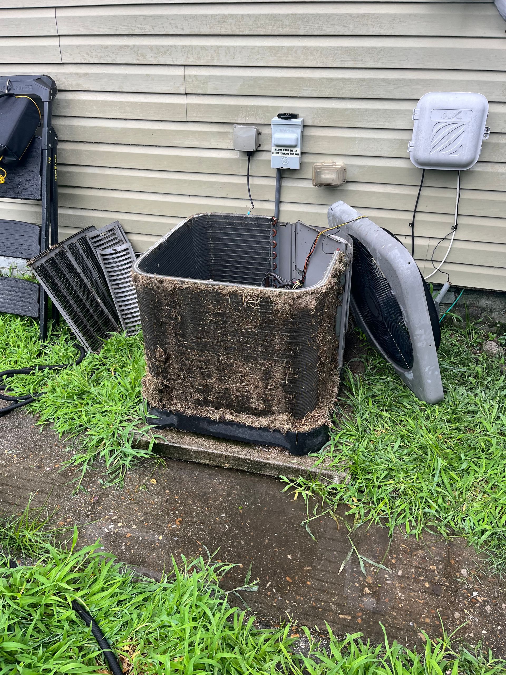 A dirty air conditioner is sitting in the grass next to a house.