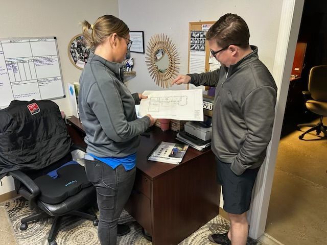 A man and a woman are standing in an office looking at a blueprint.