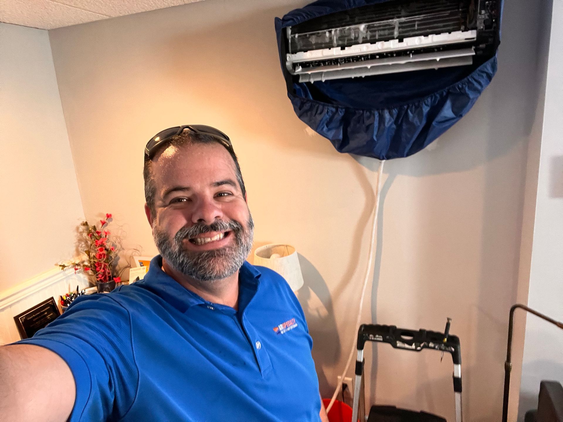 A man in a blue shirt is taking a selfie in front of an air conditioner.