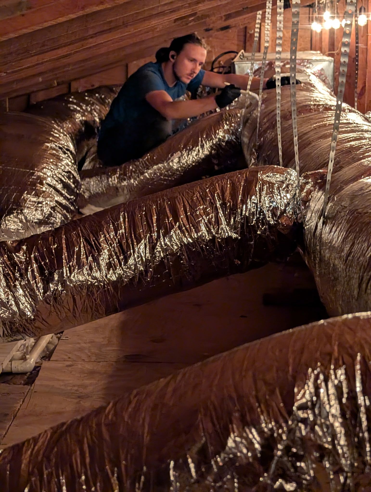 Man in attic working on silver ductwork.