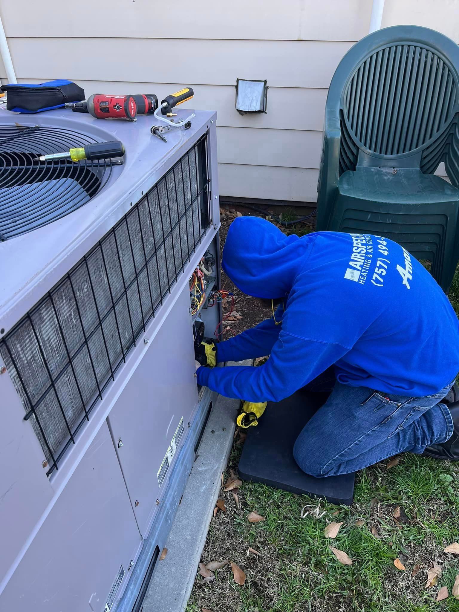 A man in a blue hoodie is working on an air conditioner.