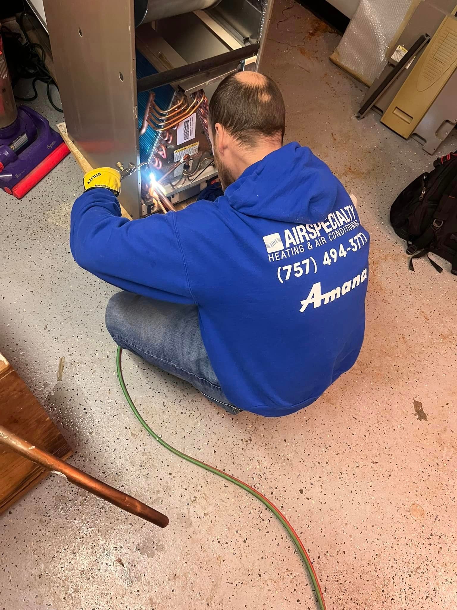 A man in a blue hoodie is welding a piece of metal in a garage.