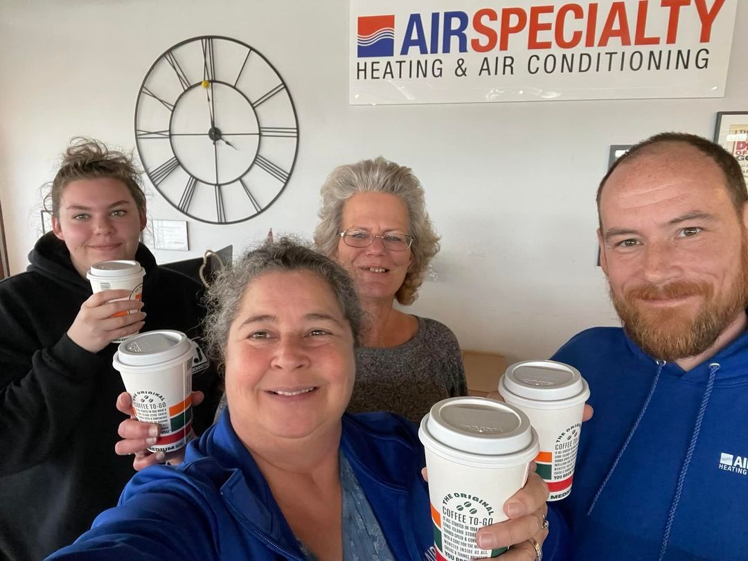 A group of people are holding coffee cups in front of a sign that says fair specialty heating and air conditioning.