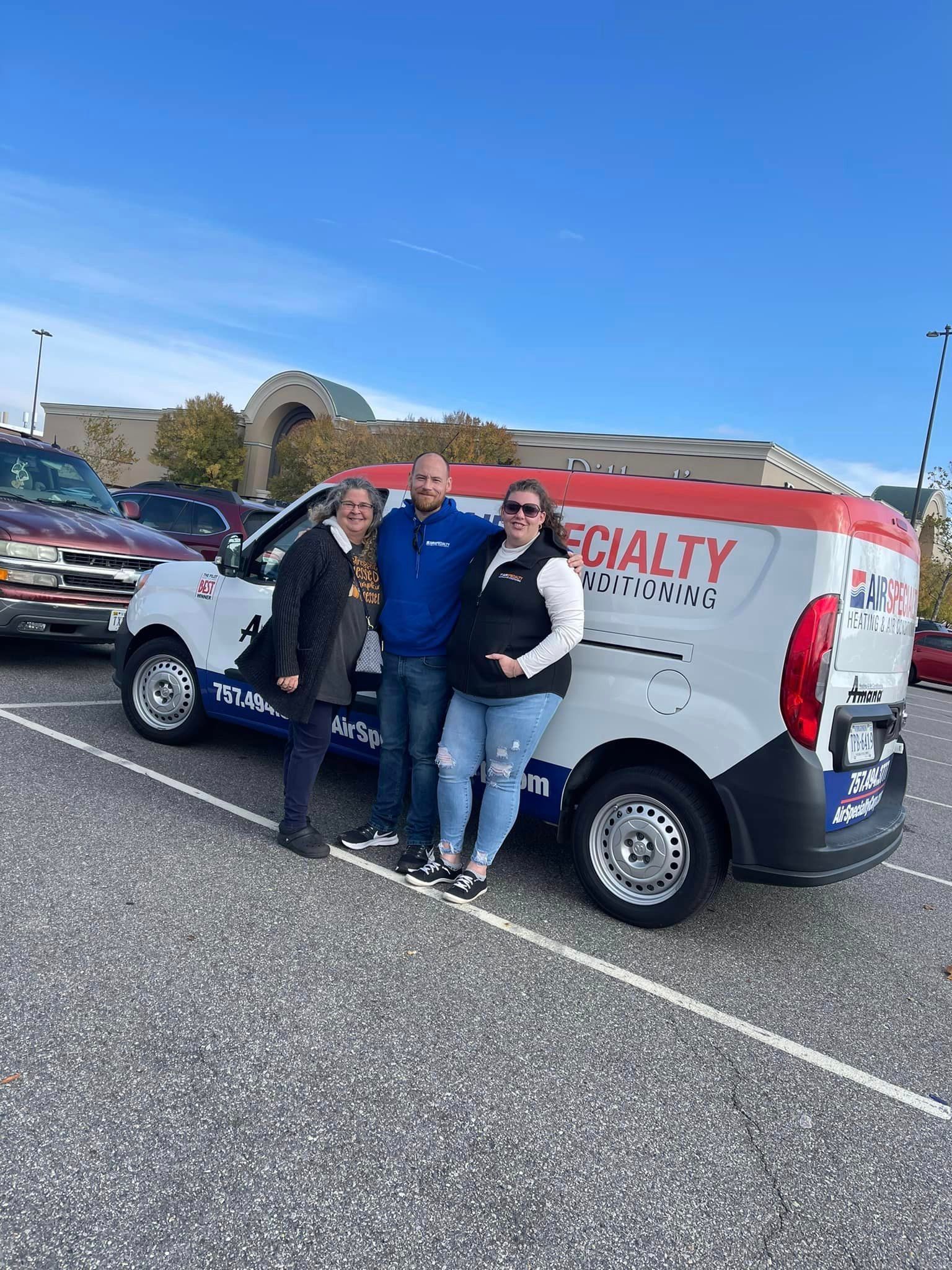 Three people are standing in front of a van in a parking lot.