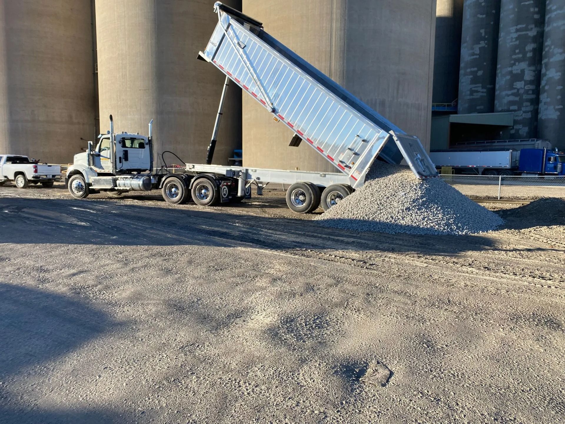 Dump truck unloading gravel beside large silos at an industrial site