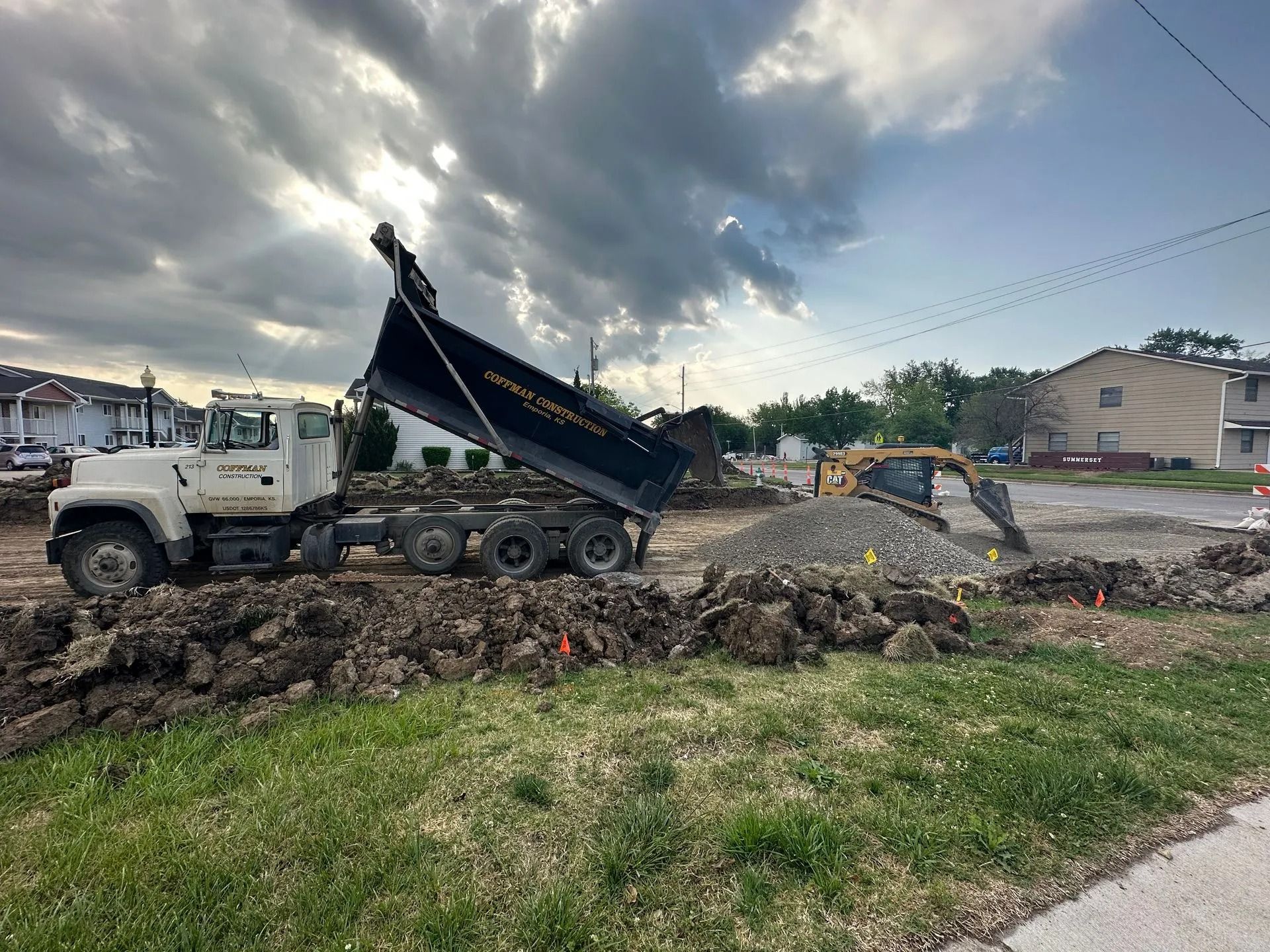 White dump truck unloading dirt at a muddy construction site with an excavator in the background