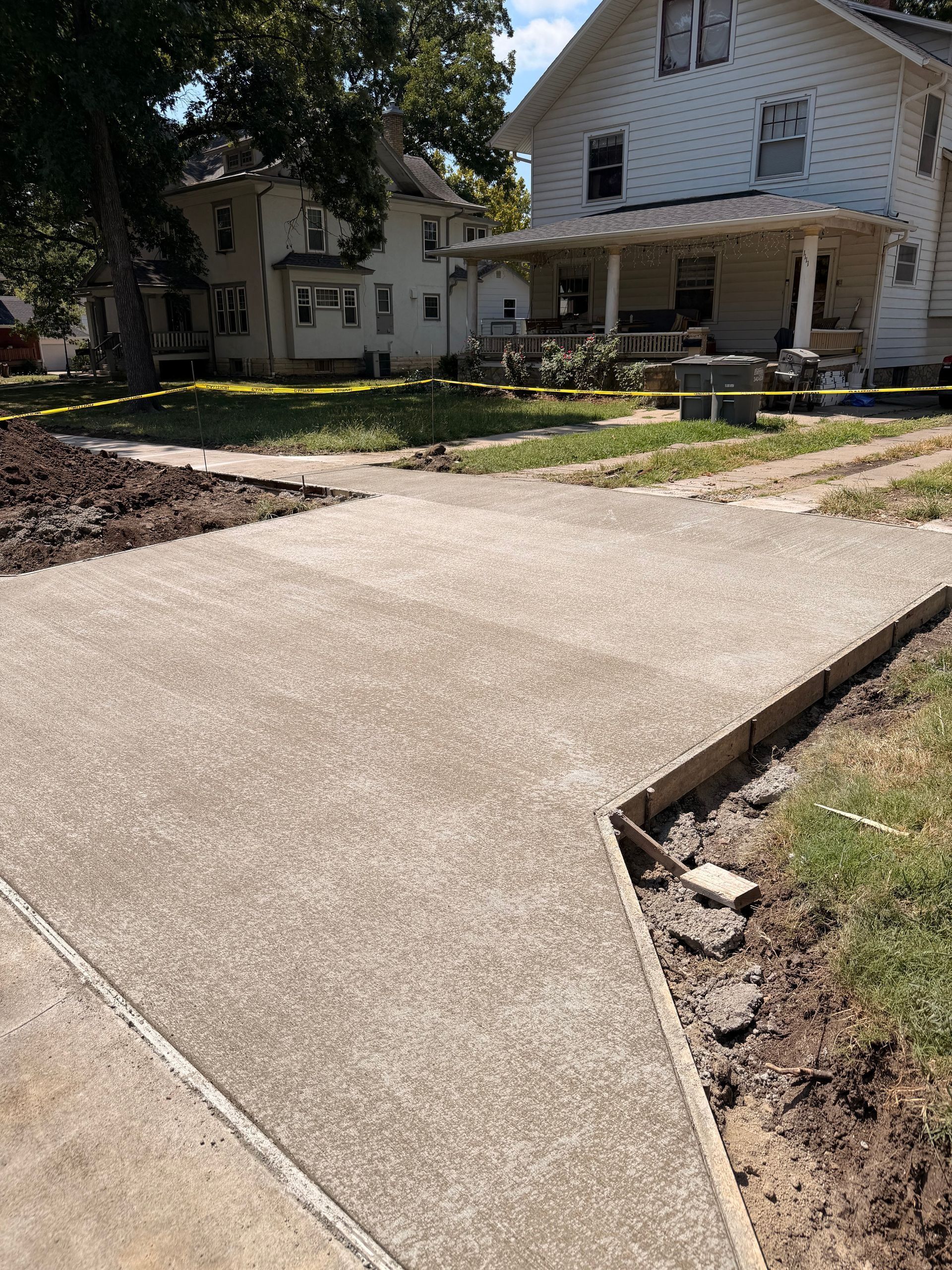 Concrete driveway leading to a white house with a front yard and yellow caution tape around the lawn.