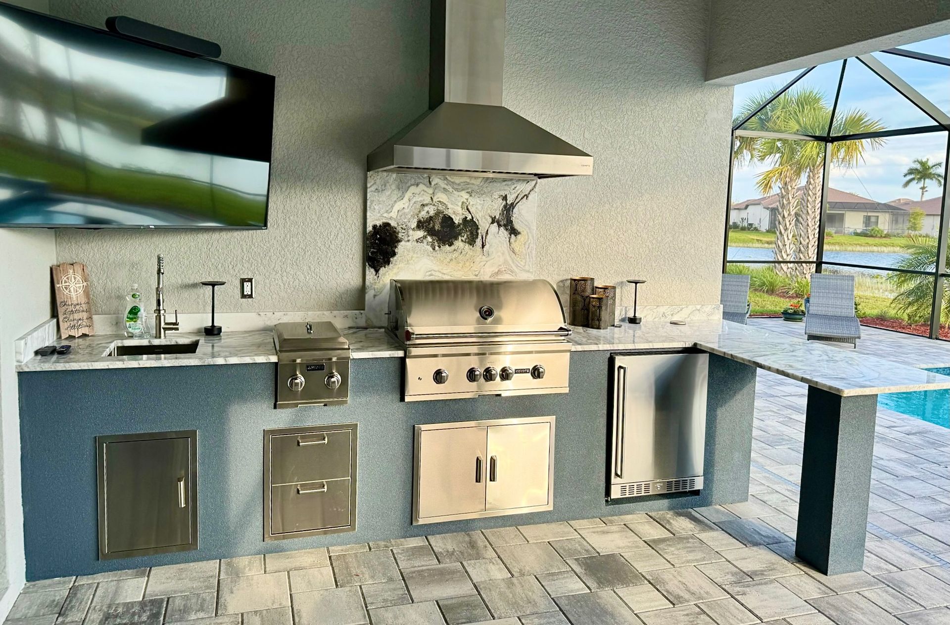 An outdoor kitchen with stainless steel appliances and a flat screen tv.