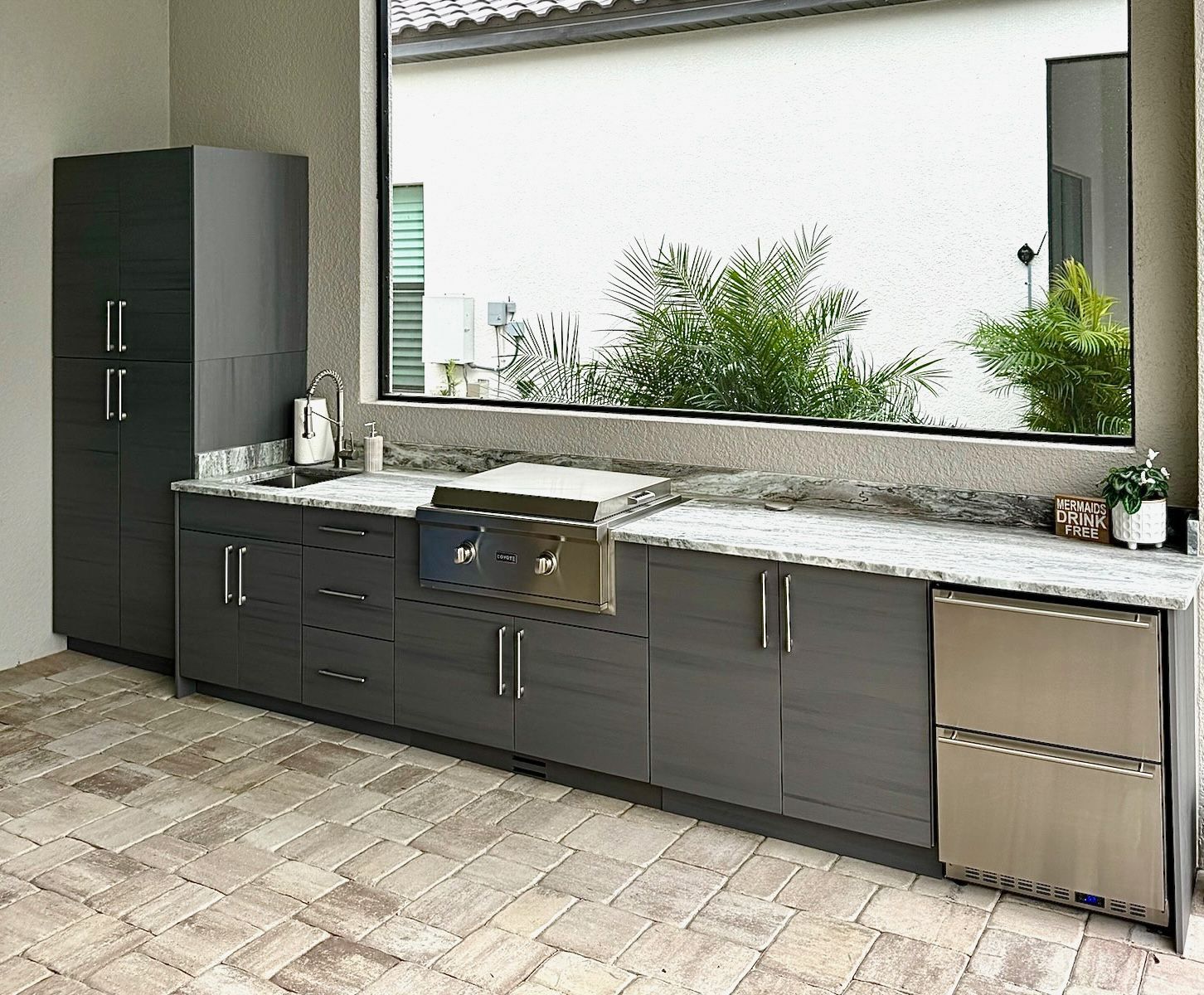 A kitchen with gray cabinets, stainless steel appliances, and a large window.