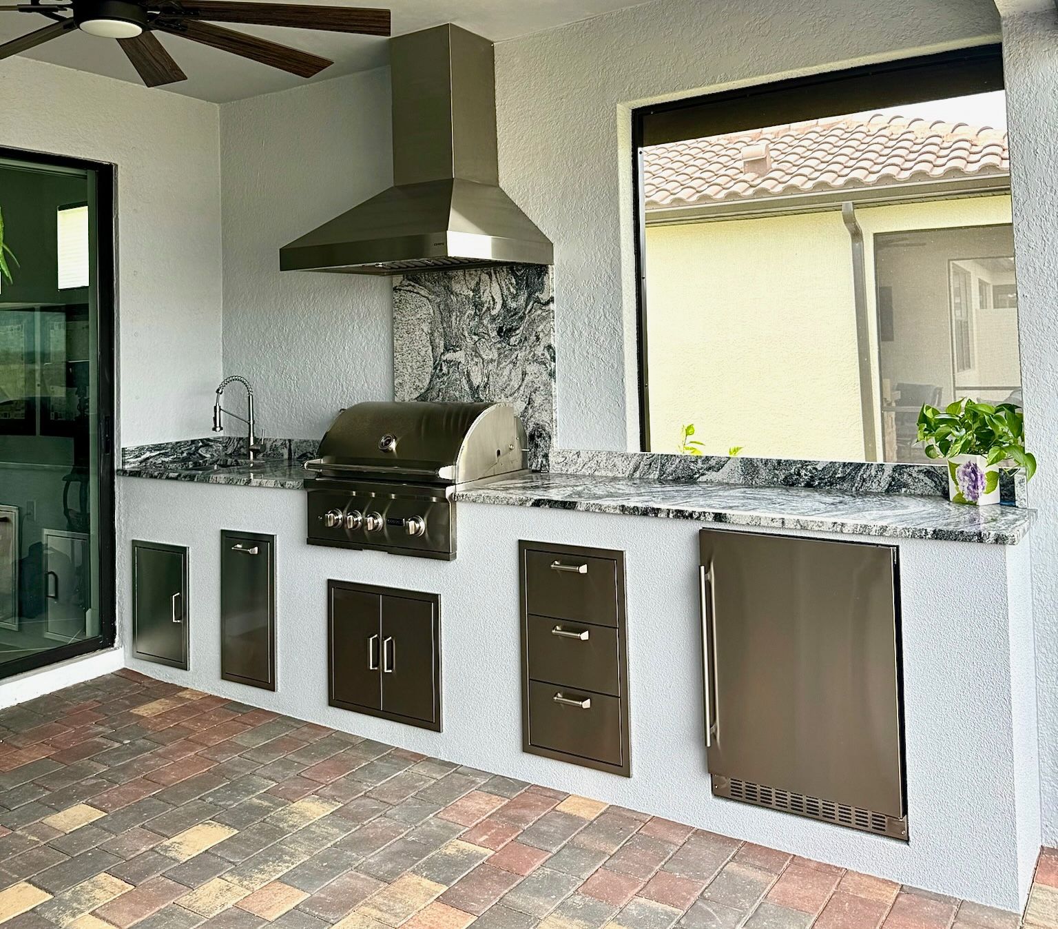 An outdoor kitchen with a grill and a ceiling fan.