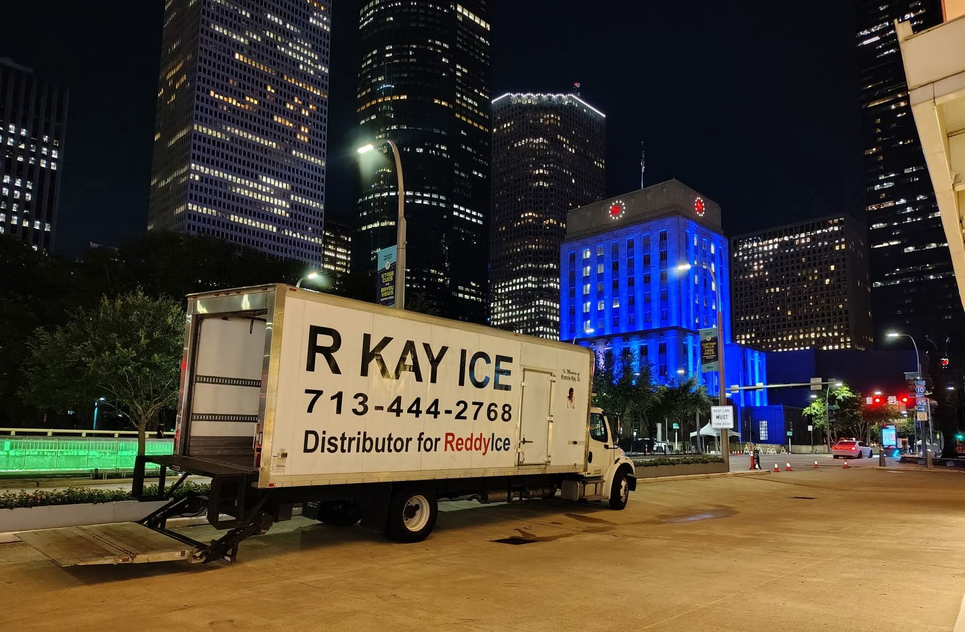 White ice truck parked on a street in a city at night; tall buildings in the background.