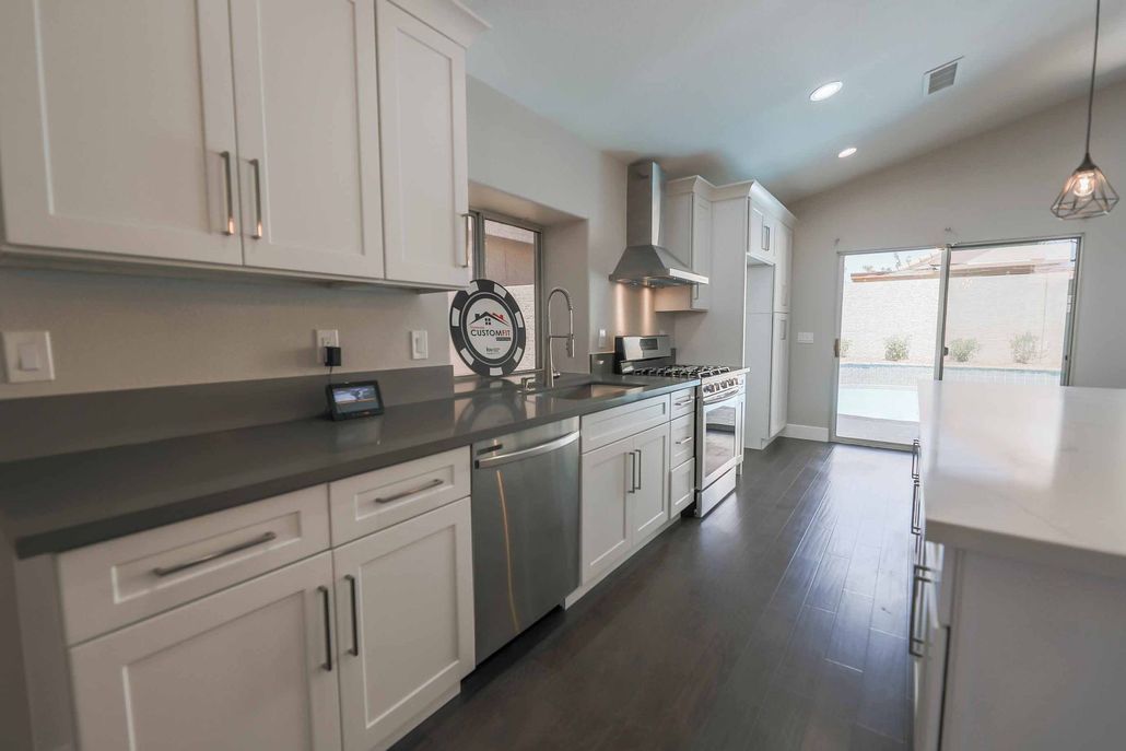 Modern white kitchen with stainless steel appliances, dark countertops, and a view of a pool.