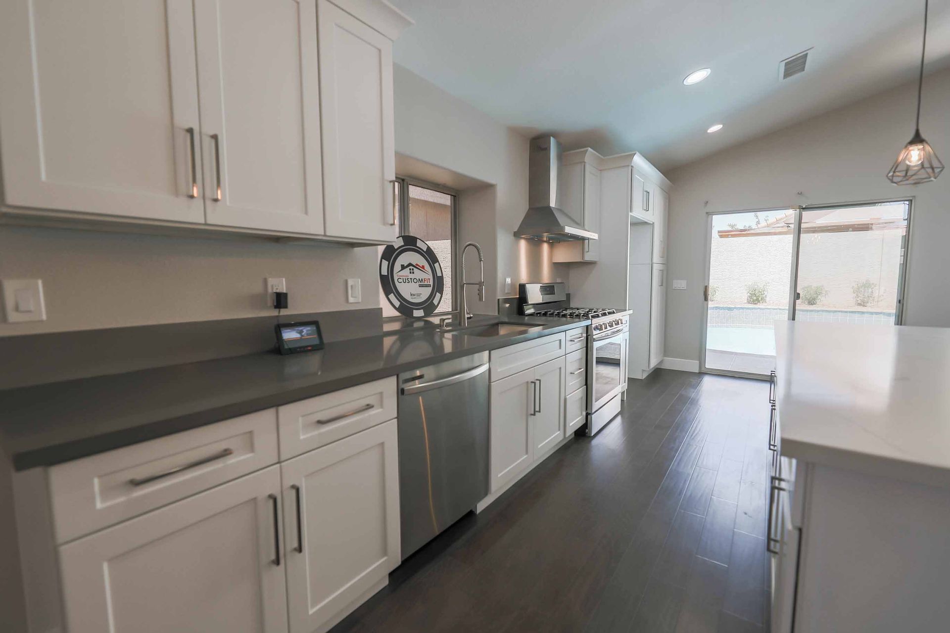 Modern white kitchen with stainless steel appliances, dark countertops, and a view of a pool.