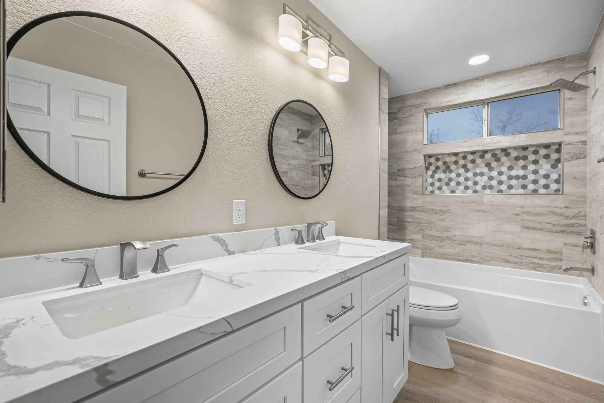 Bathroom with white double vanity, round mirrors, and a tile shower.