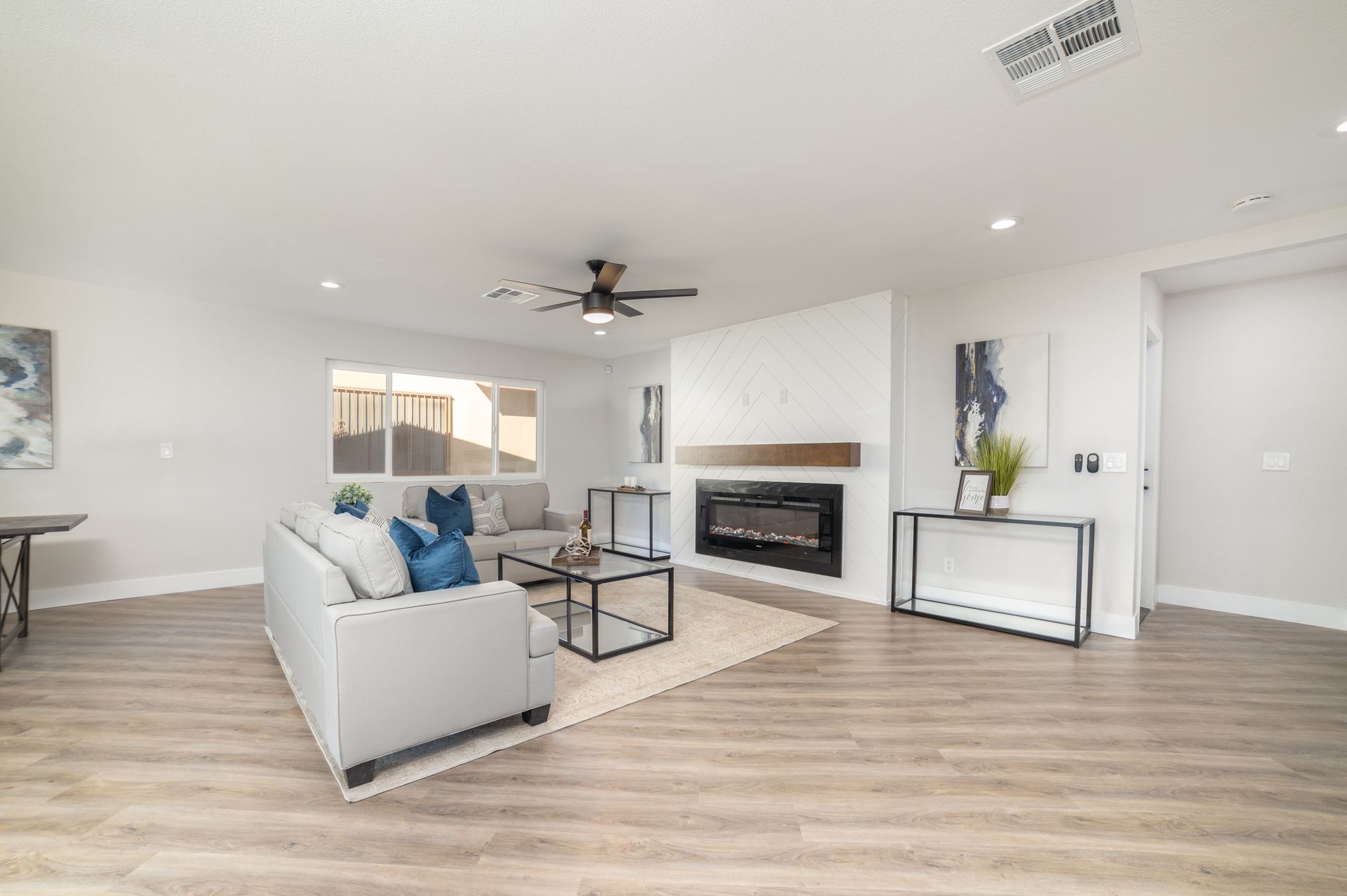 Spacious living room with white walls, fireplace, light wood floors, and neutral furniture.