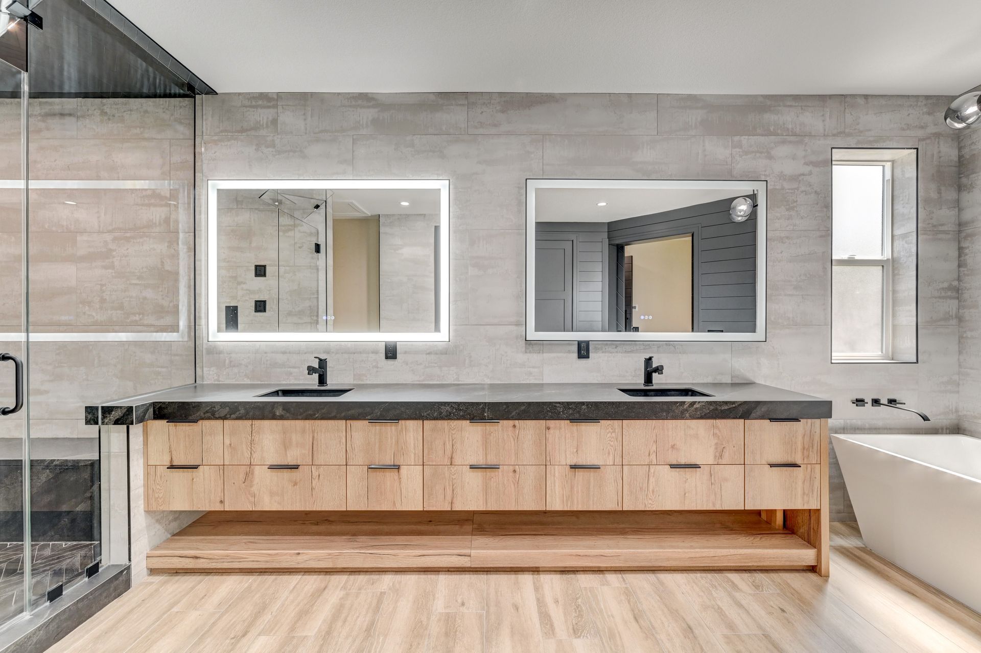 Modern bathroom with wood vanity, two mirrors, and a freestanding tub.
