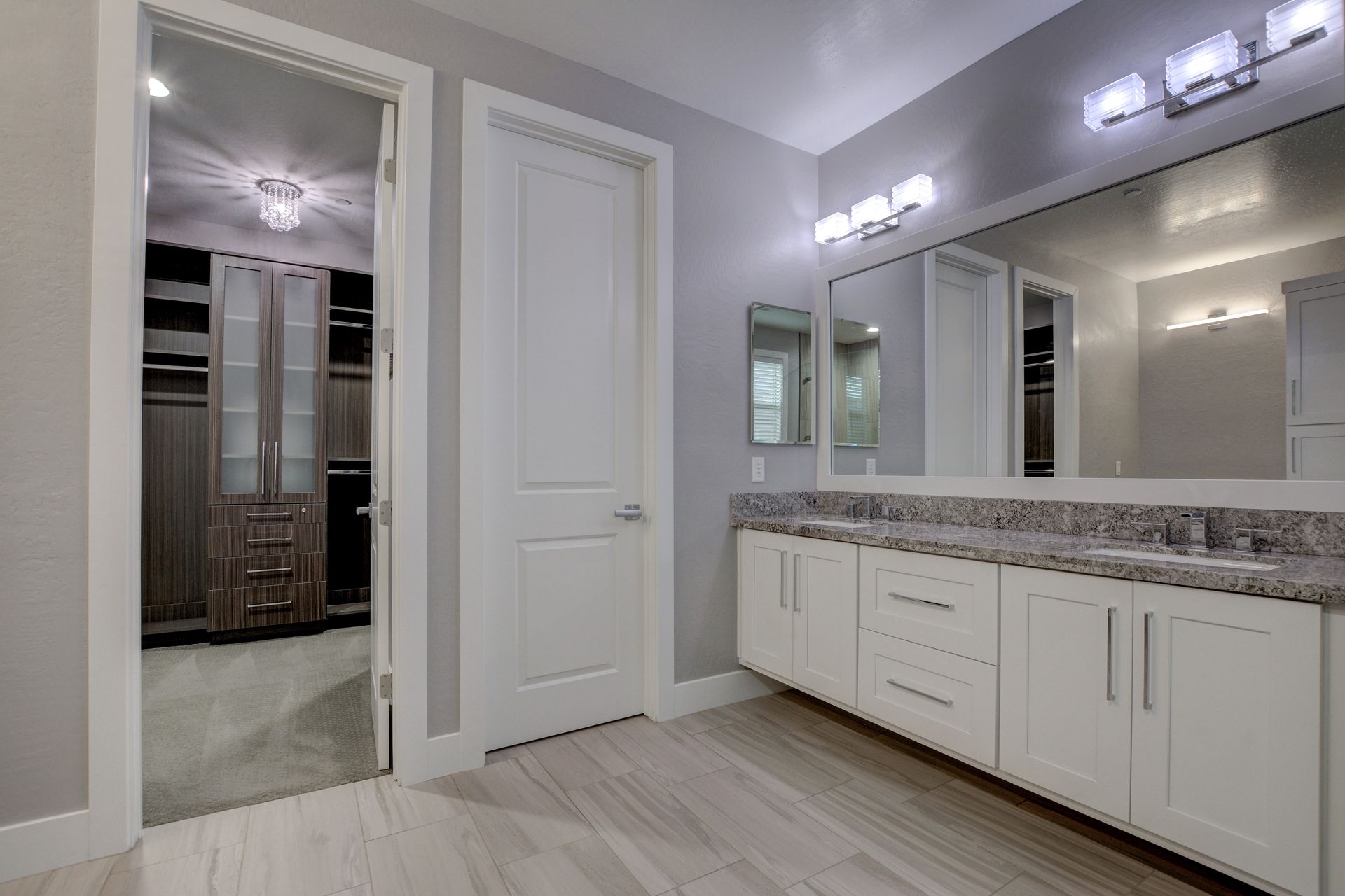 Bathroom with white vanity, large mirror, and entrance to a walk-in closet with built-in shelves and drawers.