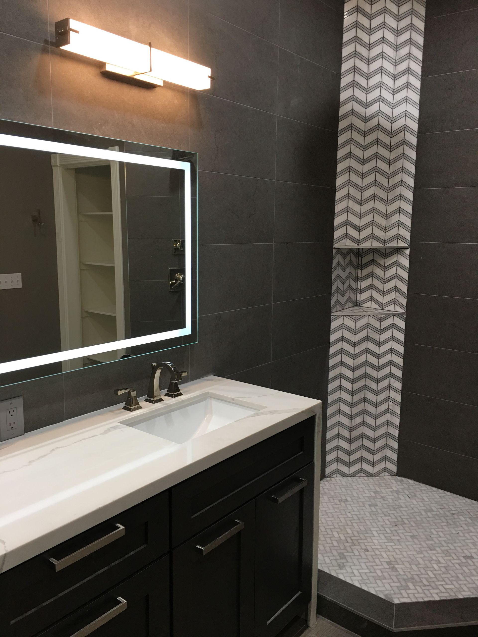 Modern bathroom with dark gray walls, white countertop, black vanity, and herringbone tile shower.