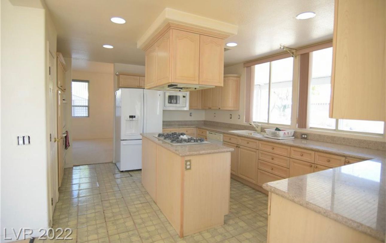 Kitchen with beige cabinets, island with stovetop, refrigerator, and windows.