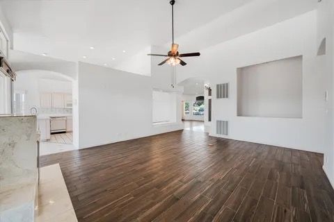Empty living room with wood floor, high ceiling, and a ceiling fan.