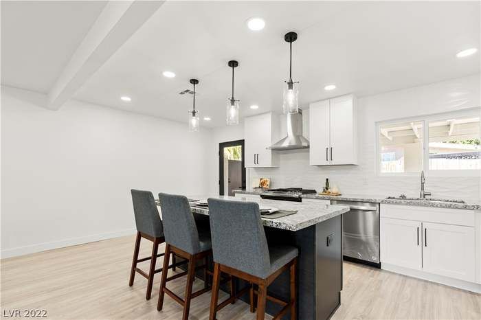 Modern kitchen with island, stainless steel appliances, white cabinets, and bar stools.