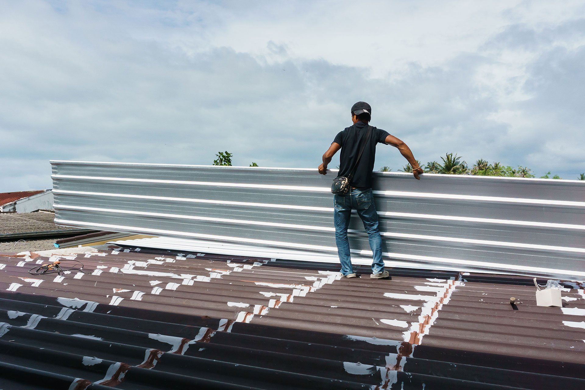 A man is standing on top of a roof holding a piece of metal.