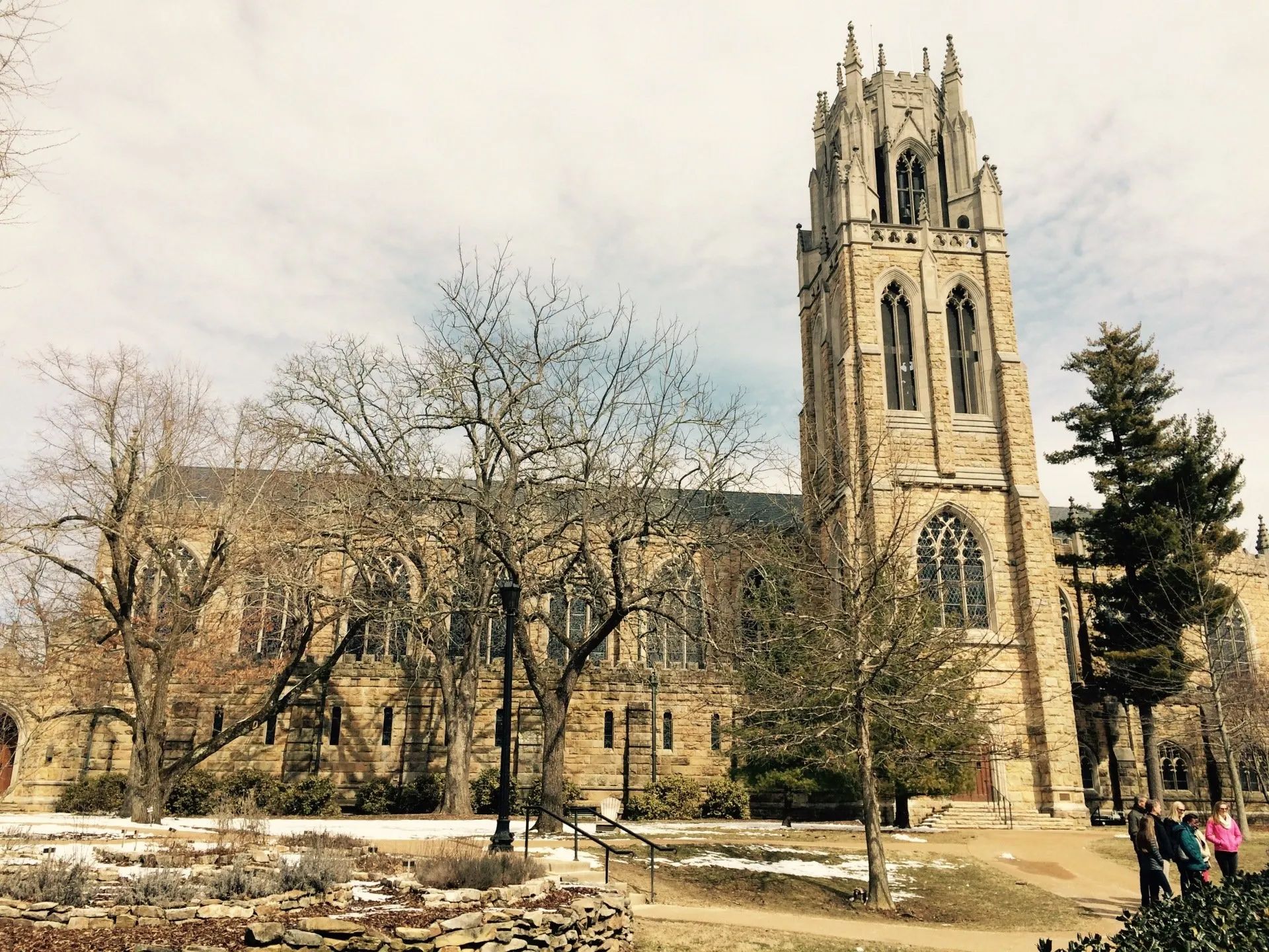 A large stone building with a clock tower is surrounded by trees.