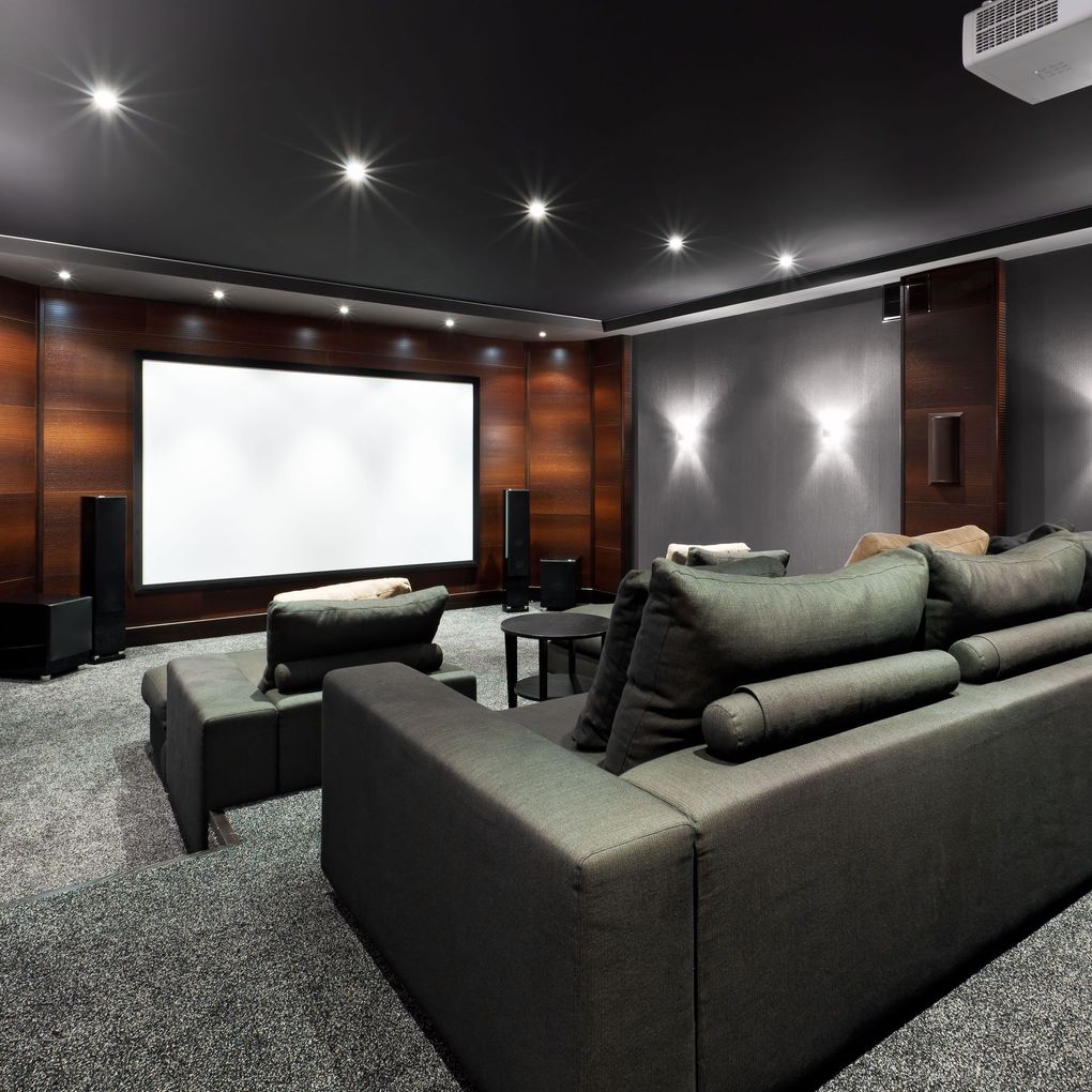 Home theater room with a recliner, screen, speakers, red carpet, and tiered seating.