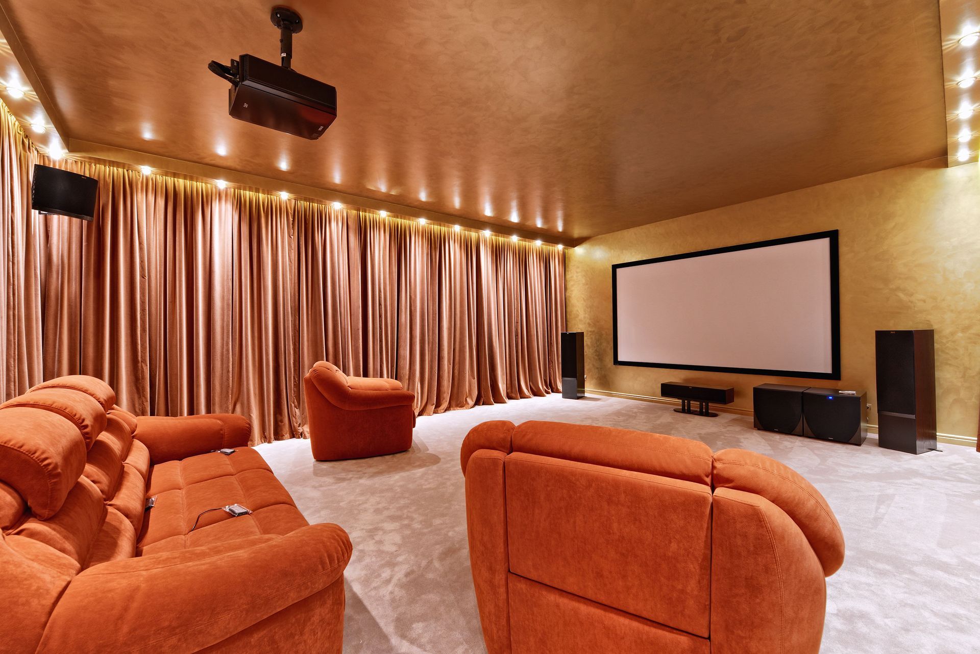 Home theater with orange seating, large screen, projector, and gold-toned walls/curtains.