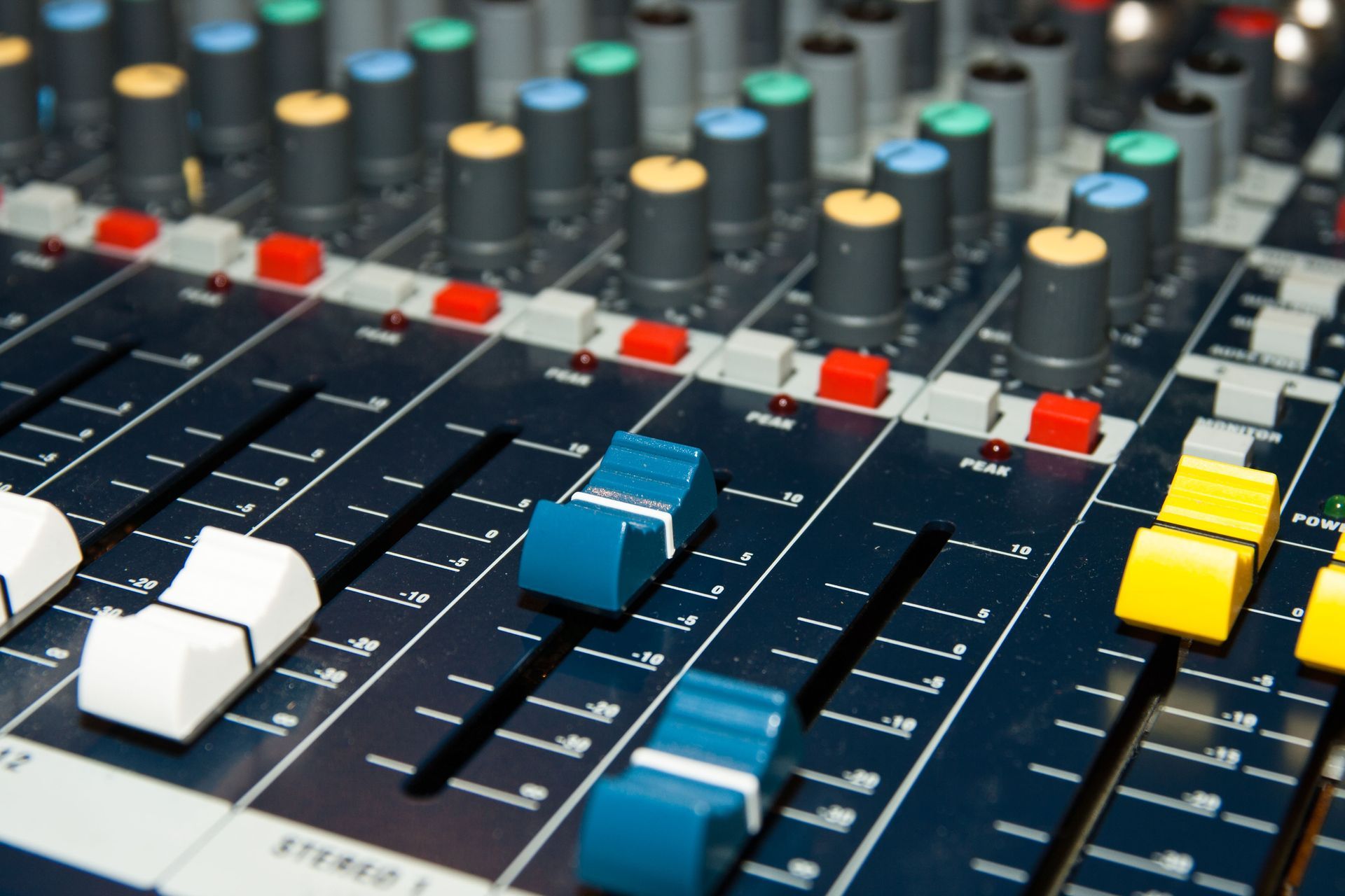 Audio mixing console with knobs, faders, and buttons; a close-up perspective.
