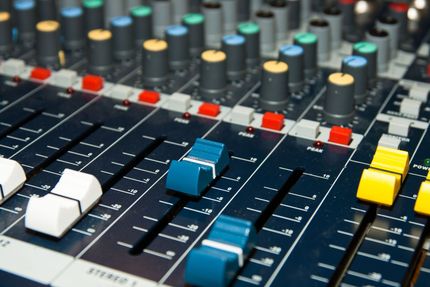Audio mixing console with knobs, faders, and buttons; a close-up perspective.