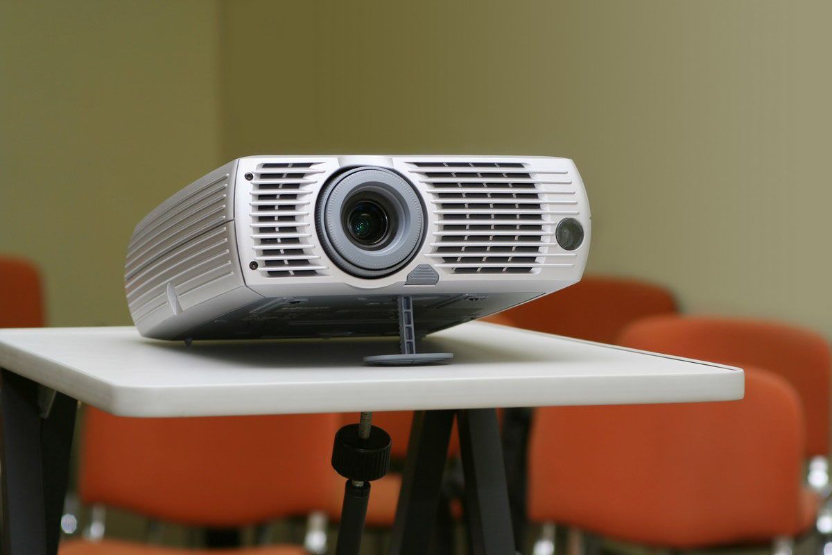 Projector on a white table in front of orange chairs.