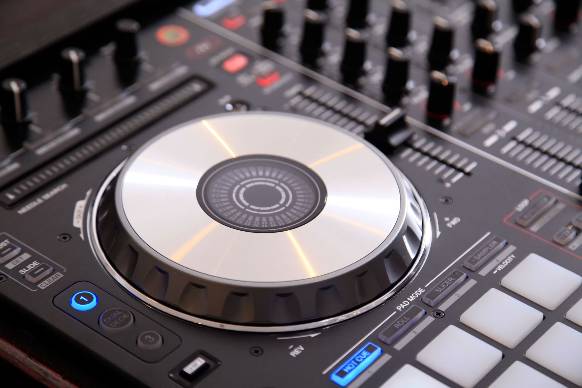 DJ mixer, close-up of a silver jog wheel, buttons, faders, and knobs. Black surface.