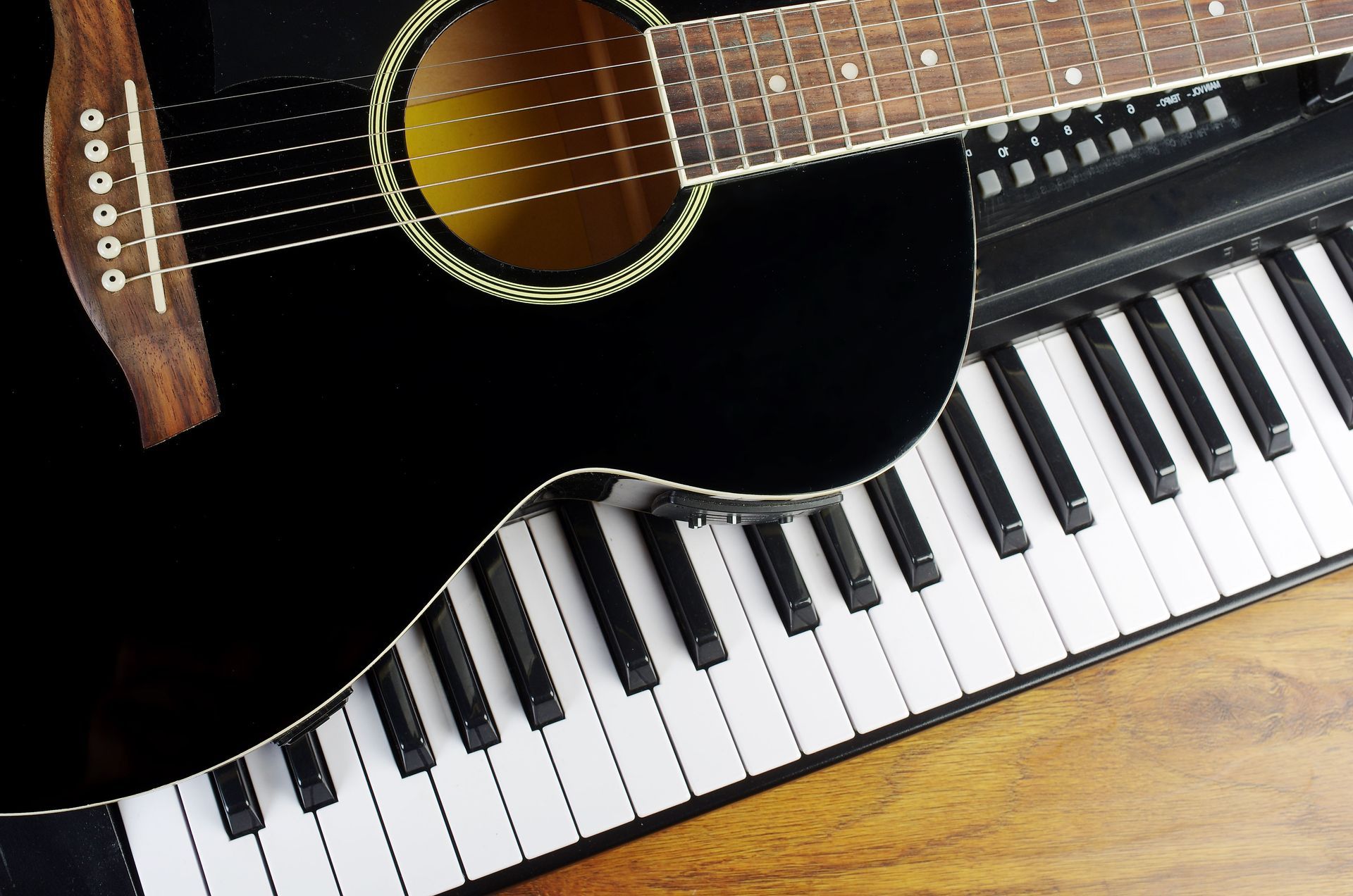 Black acoustic guitar resting on keyboard.