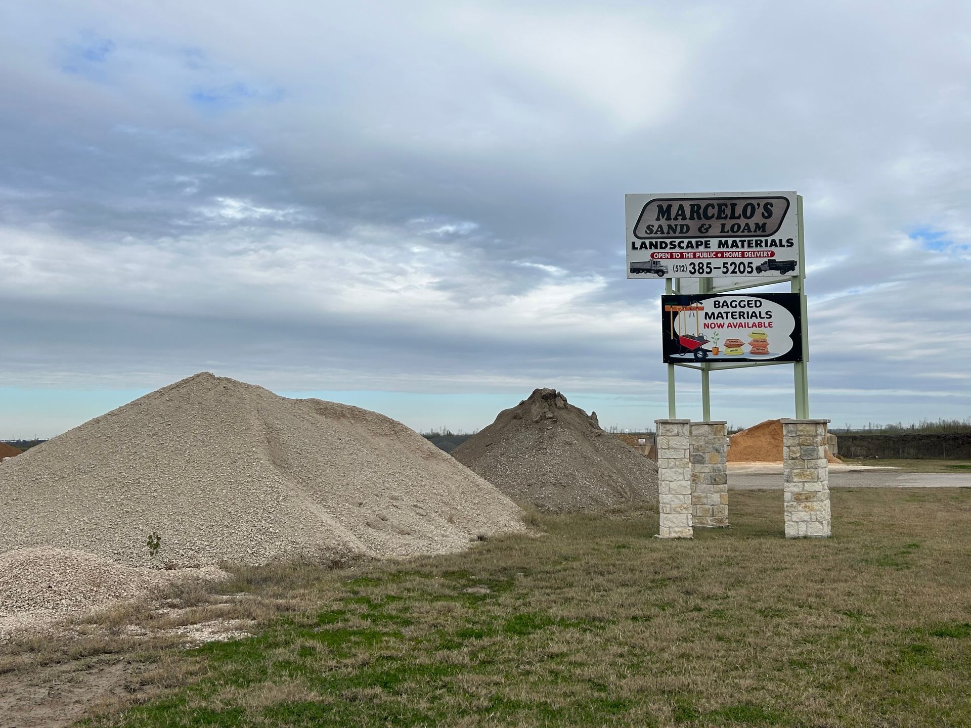 A large pile of gravel is sitting in a field next to a sign.