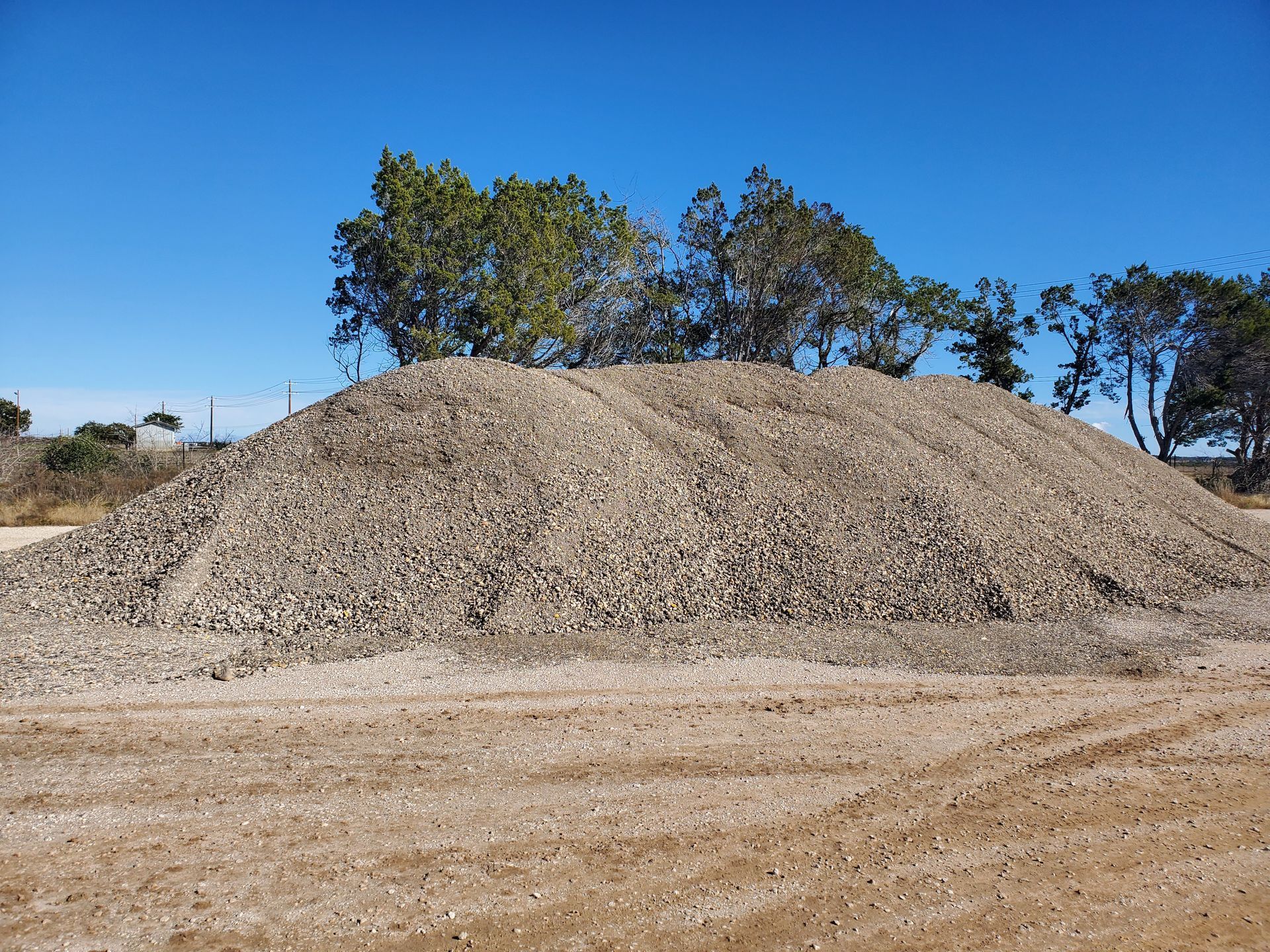 A large pile of gravel is sitting in the middle of a dirt field