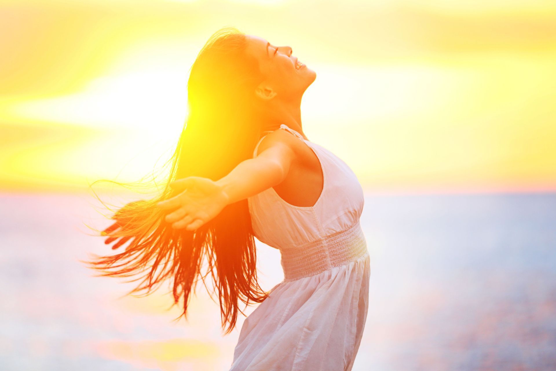 Woman standing with arms outstretched at a bright beach sunset