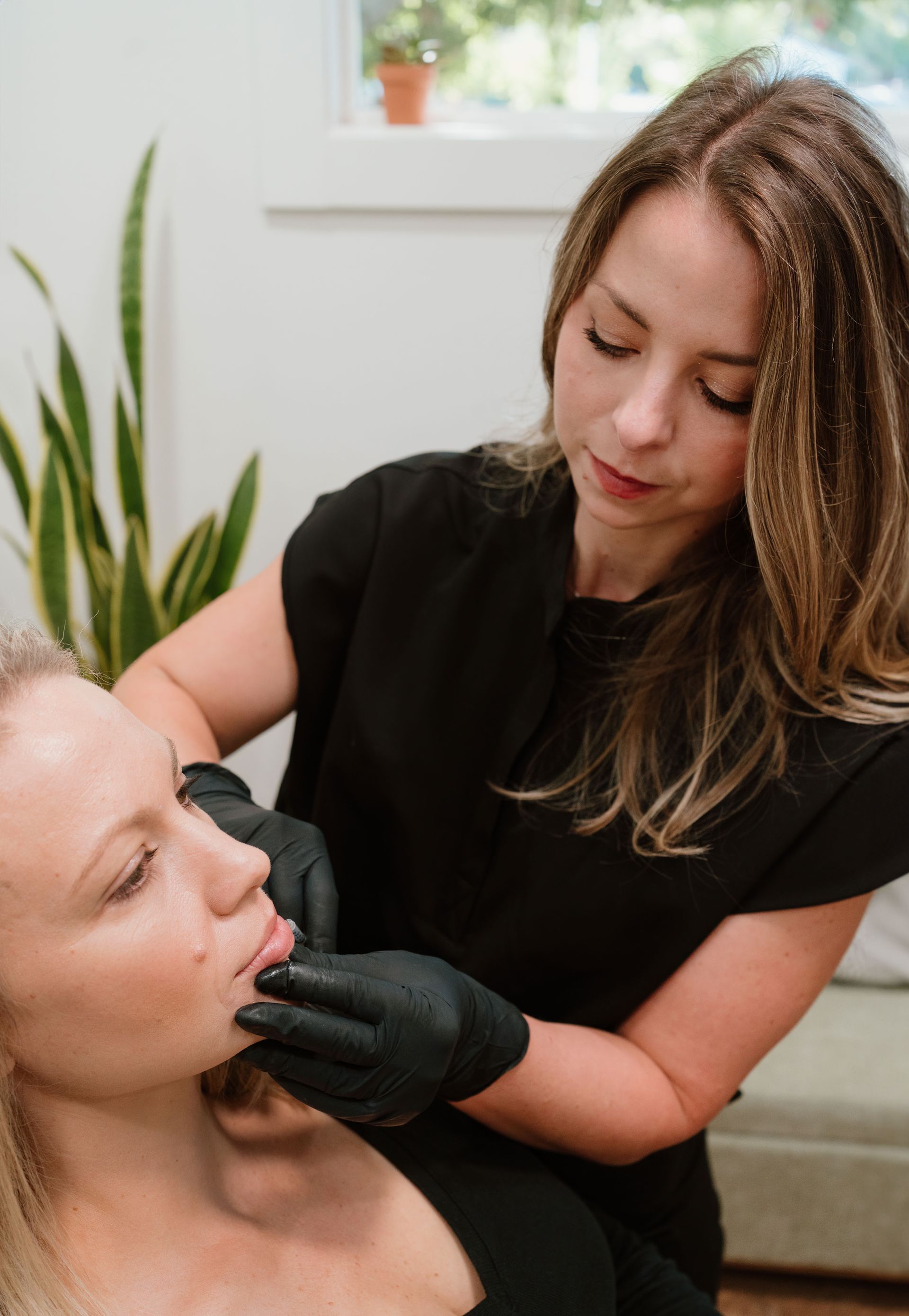 Cosmetician wearing black gloves applies treatment to a client’s face in a bright spa setting