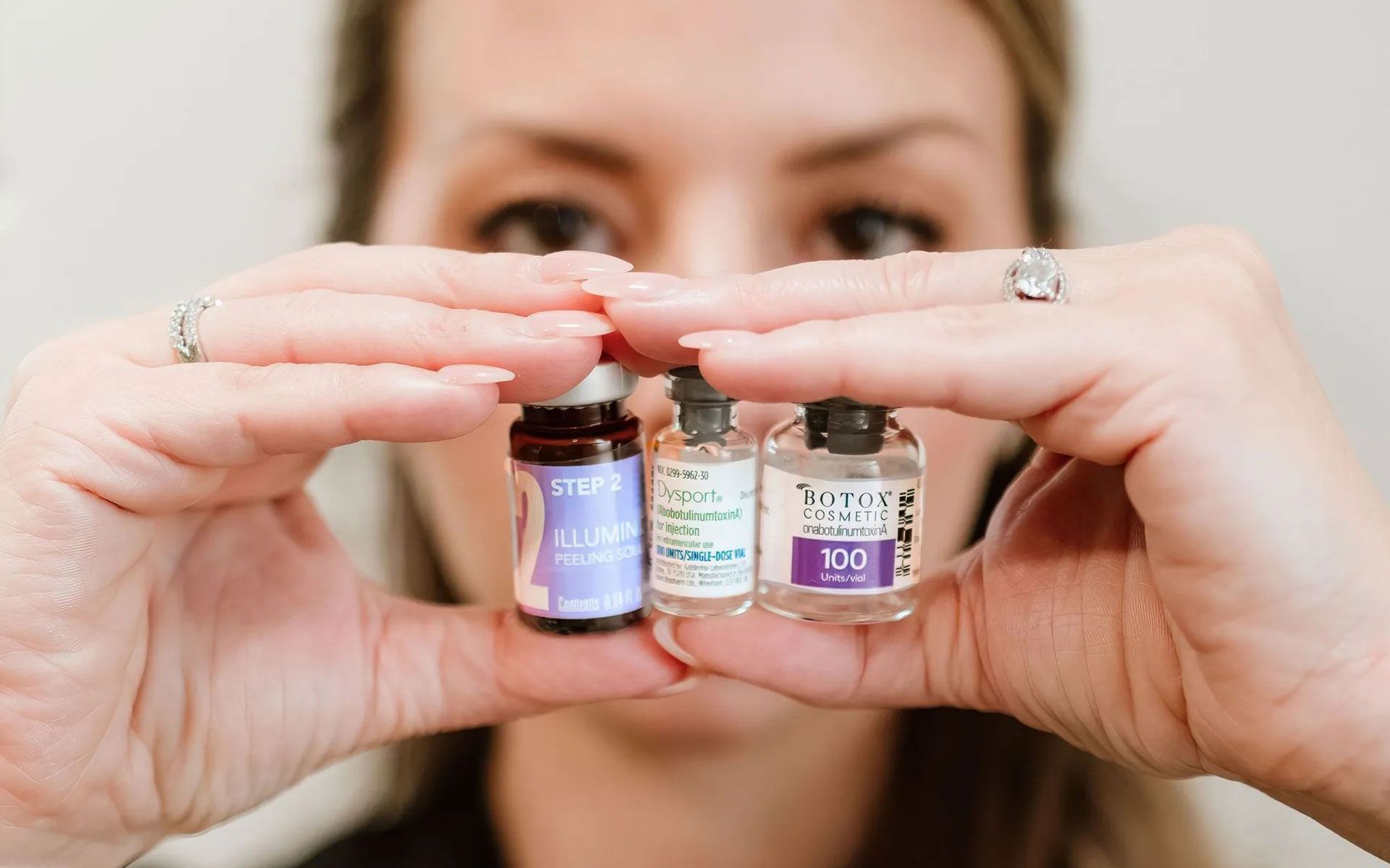 Person holding three small essential oil bottles between both hands, with face blurred in the background.